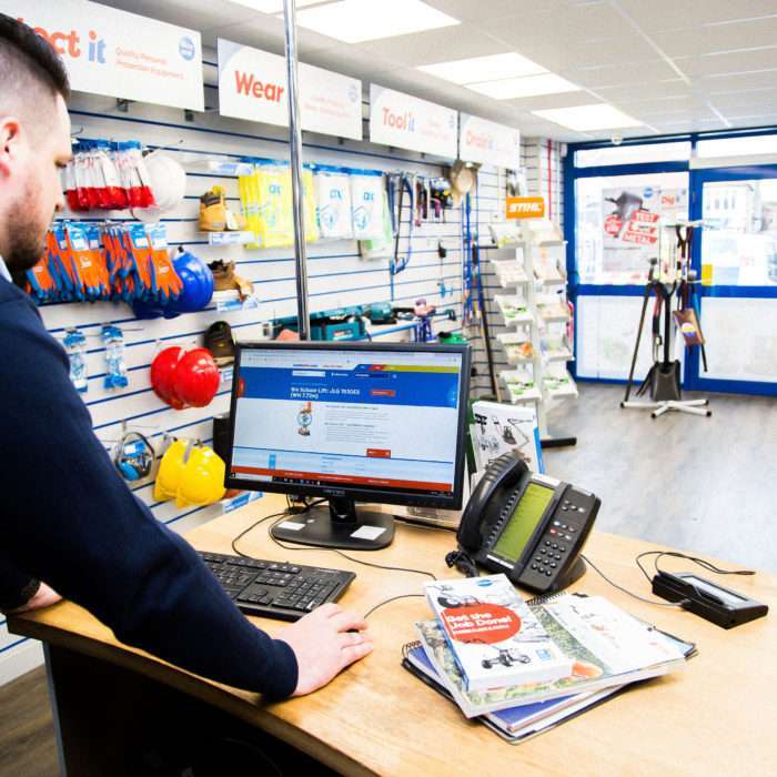 A Smiths Hire trade counter assistant in a clean, professional depot, managing an equipment hire contract on a desktop computer.